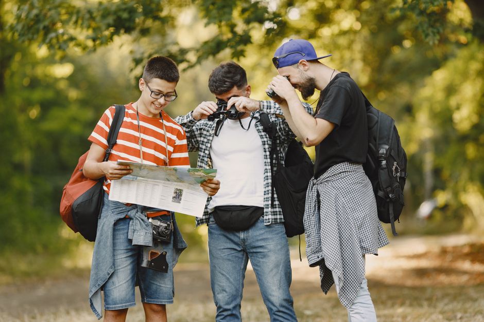 Three young men hiking and exploring a forest, using a map and binoculars.