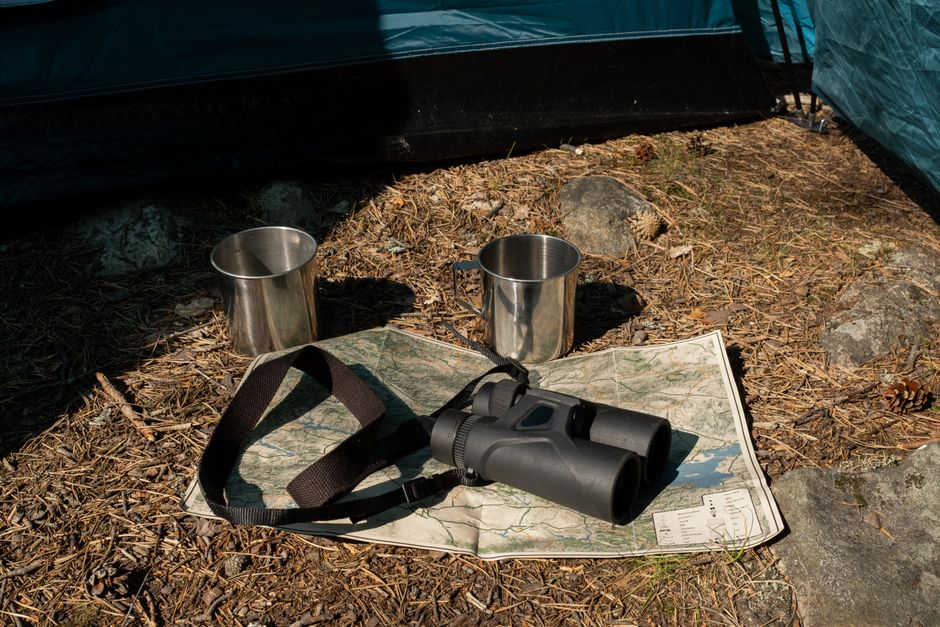 Close-up of camping gear, including binoculars, map, and cups outside a tent.