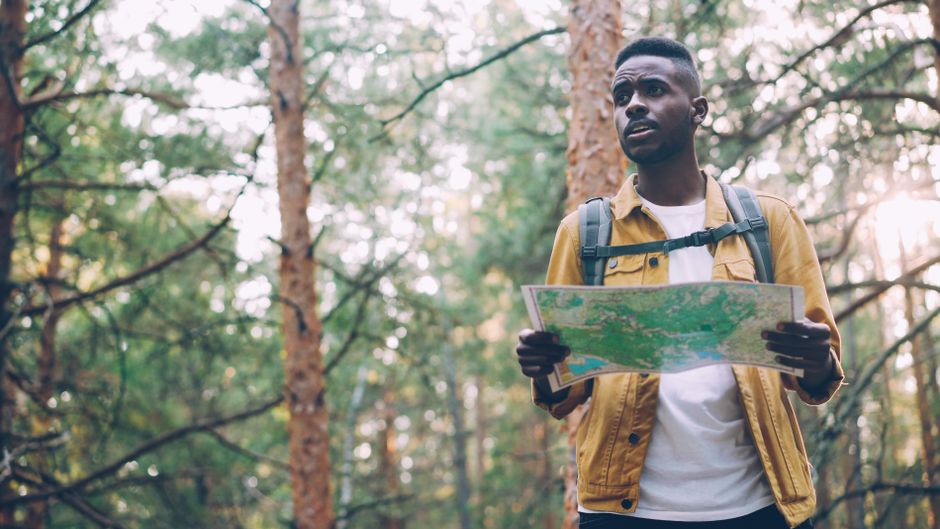 Young man with a backpack and map exploring a forest trail.