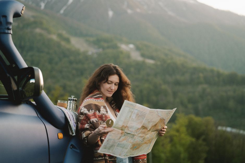A woman enjoys a scenic mountain road trip, using a map to navigate picturesque landscapes.